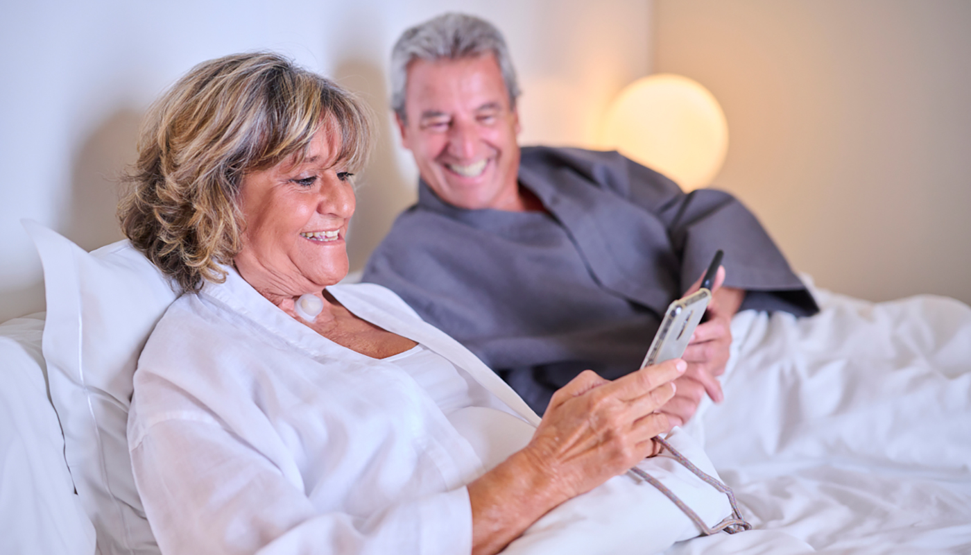 Couple in bed using phone woman with stoma